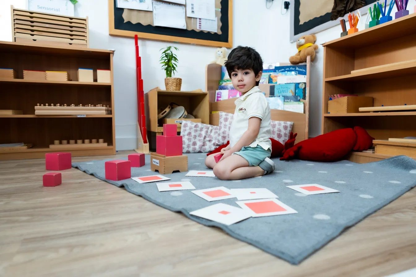 Boy arranging pink Montessori cubes on the classroom rug