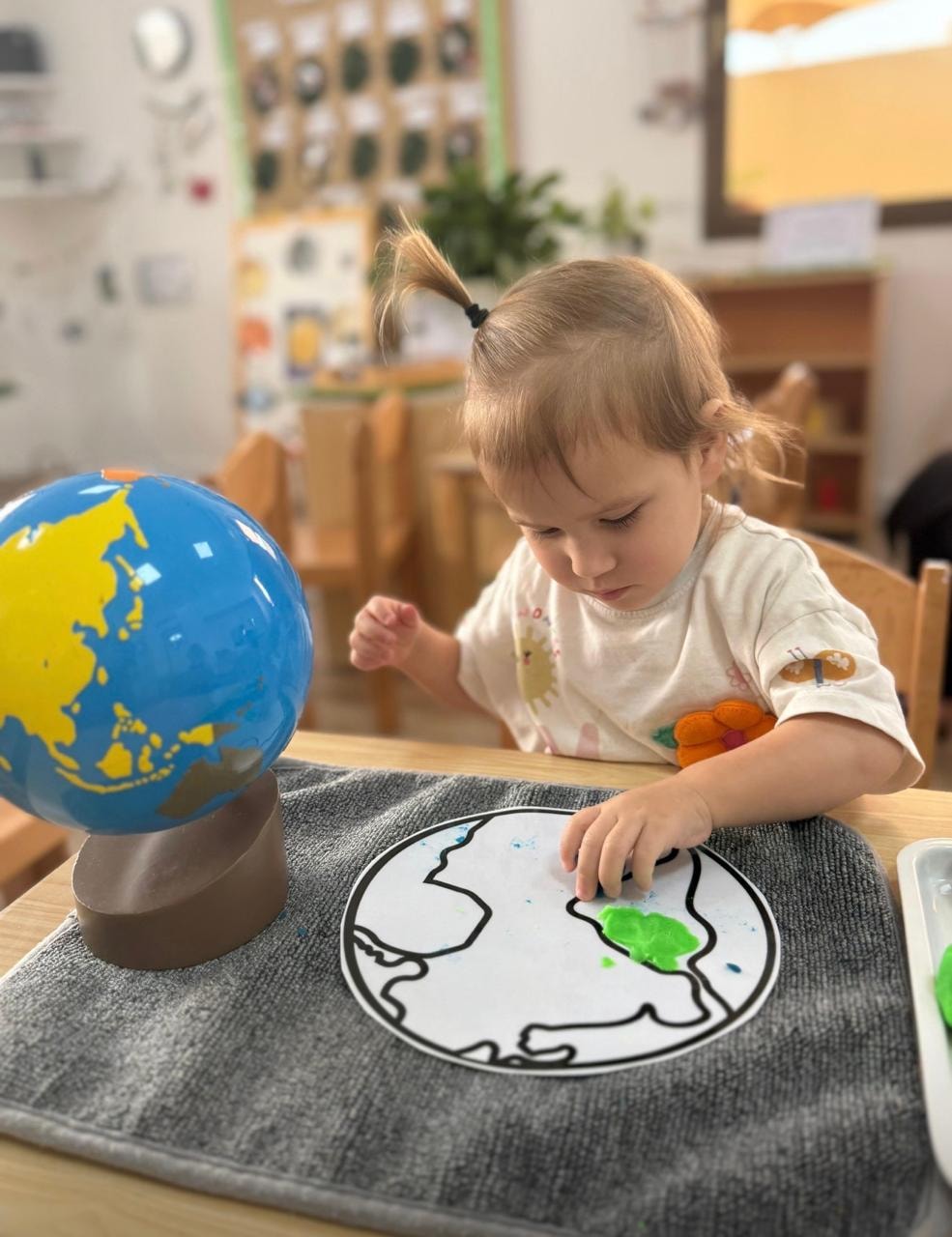 Toddler painting a globe craft activity at Ladybird Nursery